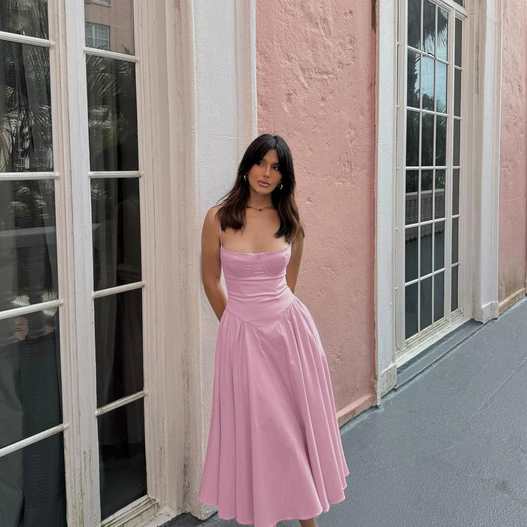 Woman in a Blush pink dress standing in front of a pink wall and glass doors.